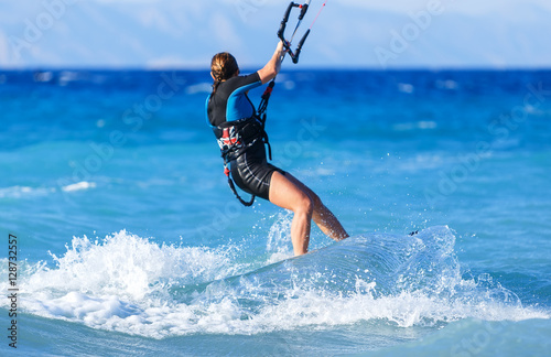young woman kite-surfer rides in greenish-blue sea under clear skies