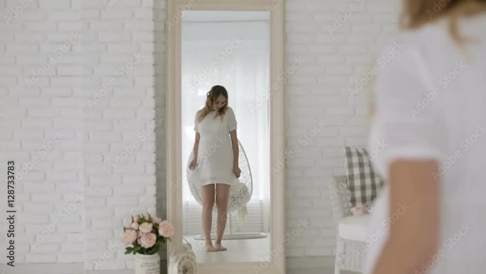 Young pregnant woman in a white dress having fun dancing in front of a mirror. Young pregnant woman in a white dress having fun dancing in front of a mirror.