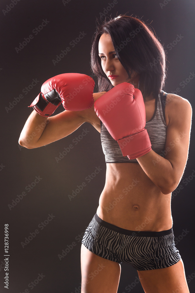 Boxing concept. Beautiful woman with red gloves on punching over black background in studio. Angry woman ready for battle or fight.