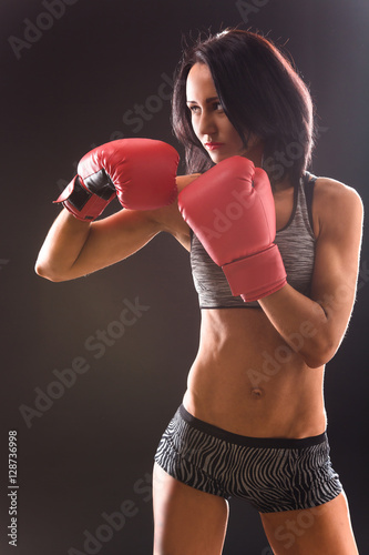 Boxing concept. Beautiful woman with red gloves on punching over black background in studio. Angry woman ready for battle or fight.