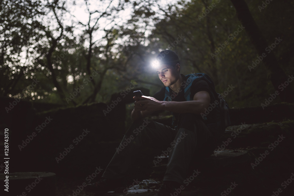 Hiker with a headlamp in the forest looking on smartphone Hiker with a headlamp in the forest looking on smartphone