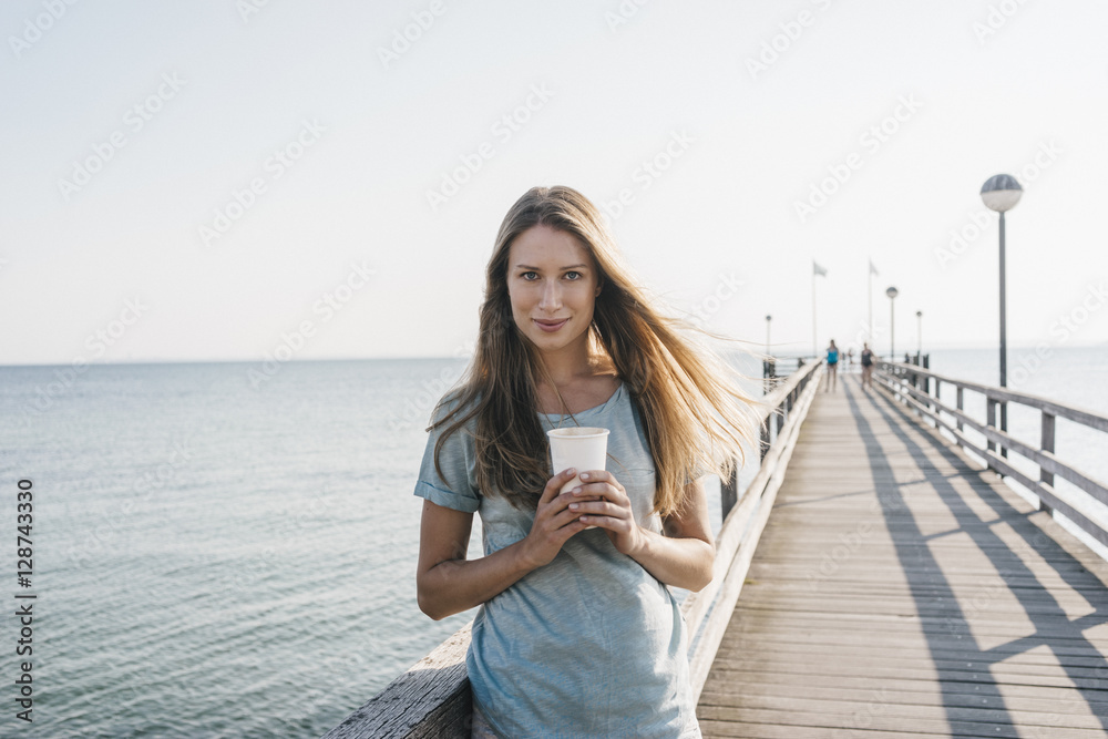 Portrait of happy young woman with coffee to go on jetty Portrait of happy young woman with coffee to go on jetty