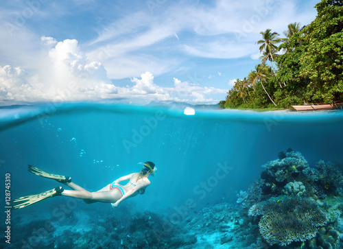 Young woman snorkeling in clear tropical waters in near of exotic island.
