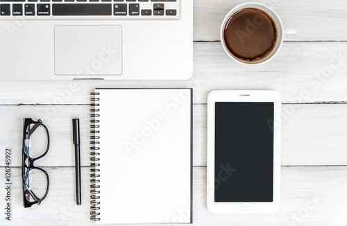 White office desk with laptop, smartphone, and notebook on wooden table. Top view with copy space. Student or business accessories flatlay. Office supplies and gadgets on background. View from above.