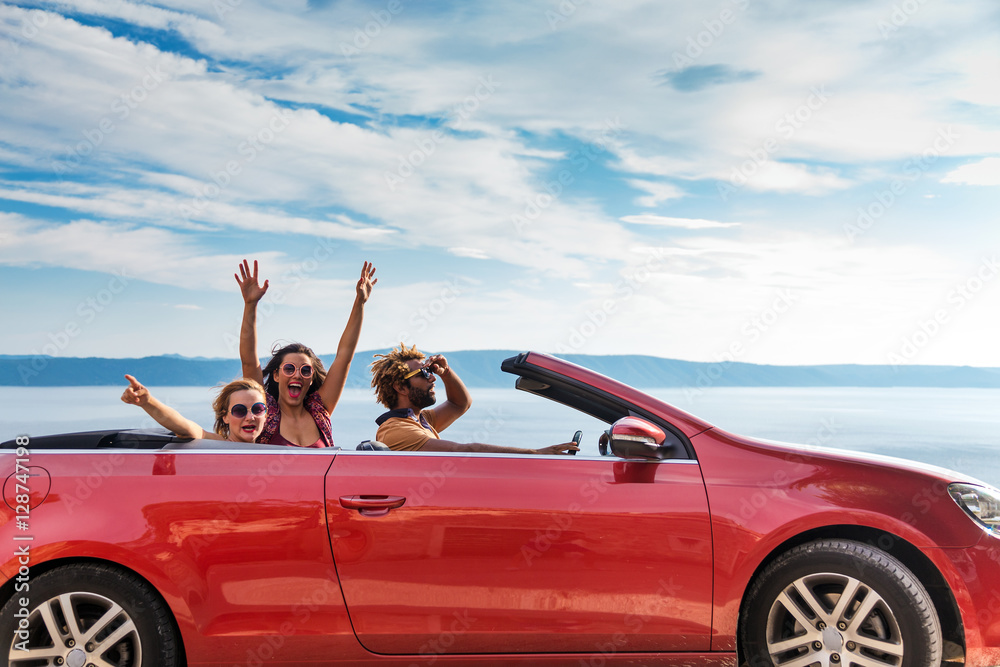 Group of happy young people waving from the red convertible. - obrazy, fototapety, plakaty 