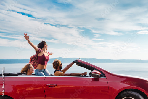 Group of happy young people waving from the red convertible. © paul prescott