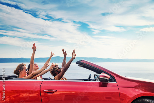 Obraz na płótnie Group of happy young people raising hands to the air in the red convertible. w salonie