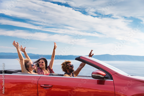 Group of happy young people waving from the red convertible. © paul prescott