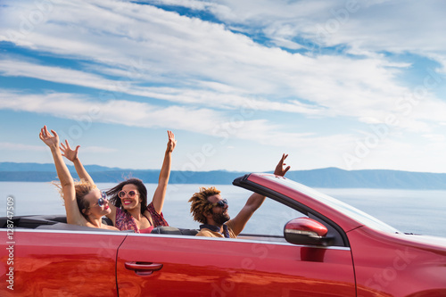 Group of happy young people waving from the red convertible.