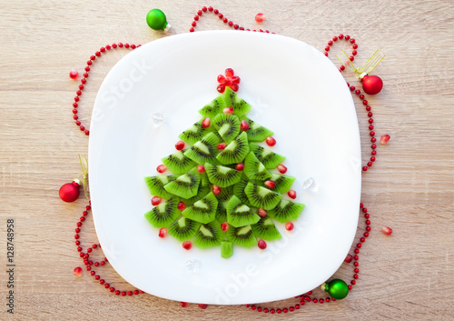 Christmas healthy dessert idea for kids party - funny edible kiwi pomegranate Christmas tree, beautiful New Year background, top view blank space for text
