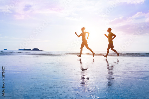 Healthy lifestyle. Young couple are jogging on beautiful sunset sea beach. Sporty family concept.