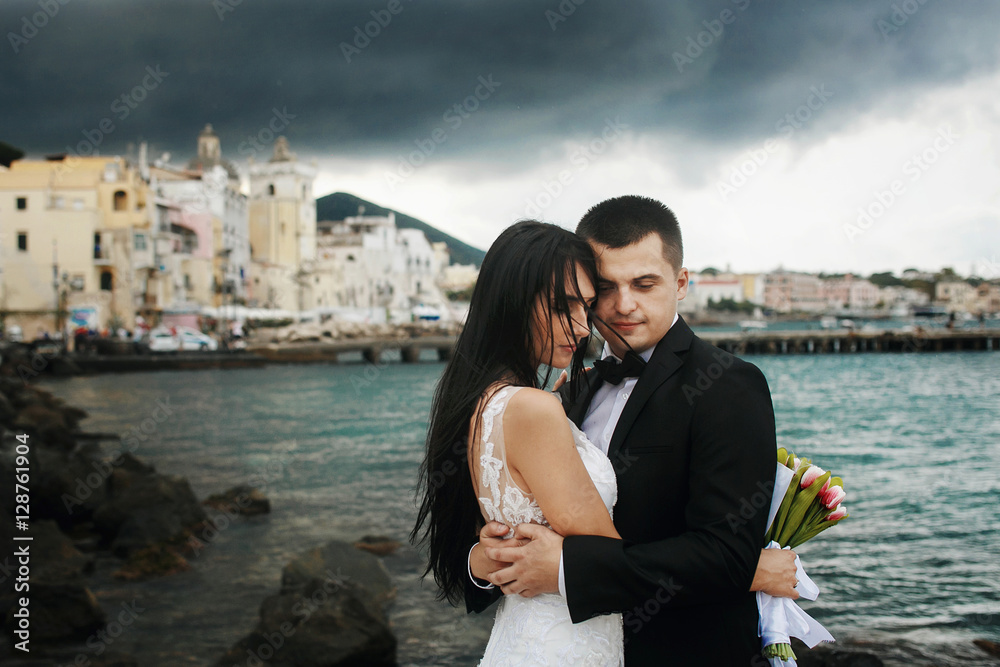 Soft embraces of lovely wedding couple standing on the rocks by Soft embraces of lovely wedding couple standing on the rocks by