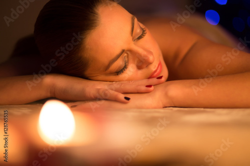 Beautiful woman lying and relaxing after spa massage by candle light
