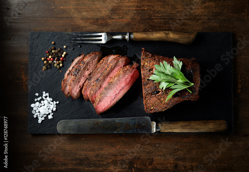 grilled steak on a black slate, knife and fork. 