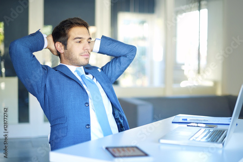 Fotografi Shot of a satisfied young businessman with hands on nape sitting in the office in front of his laptop after a well done job
