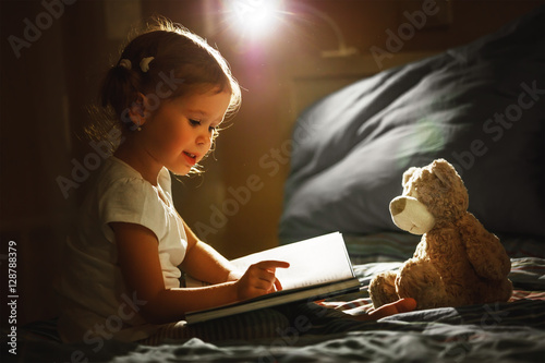 child girl reading a book in bed photo