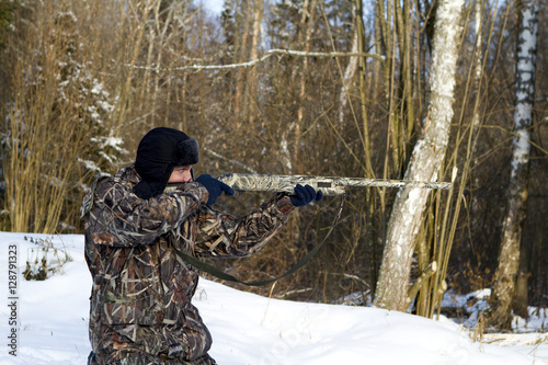 Hunter in camouflage, kneeling, taking aim a gun. season winter