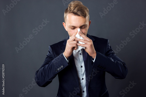 Portrait of handsome businessman having flu. Man blowing nose standing on gray background and