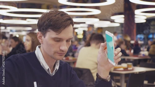Young men using smartphone and drinking coke at food court in shopping mall. Portrait