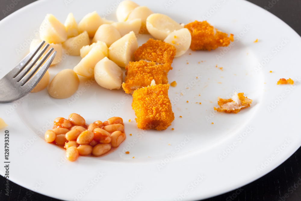 A kids dinner of potatoes, baked beans and fish fingers that has been half eaten A kids dinner of potatoes, baked beans and fish fingers that has been half eaten