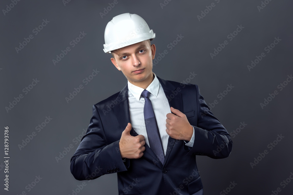 Handsome businessman in a helmet standing on gray background and straightens his jacket Handsome businessman in a helmet standing on gray background and straightens his jacket