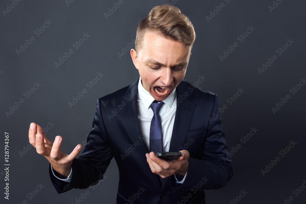 Handsome businessmanand looking in phone .and shouts standing on gray background Handsome businessmanand looking in phone .and shouts standing on gray background