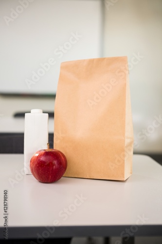 Apple with drink bottle and paper bag on table in classroom