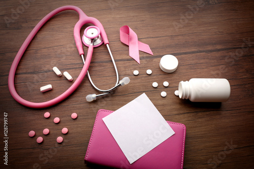 Pink stethoscope and pills on wooden background. Breast cancer concept