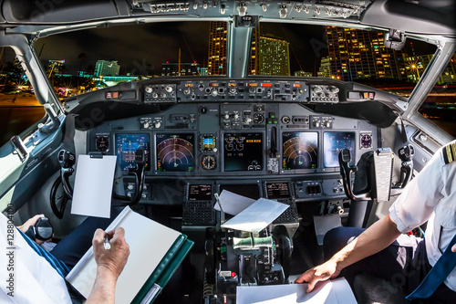 Airplane cockpit flying on Honolulu skyline by night, Oahu, Hawaii, with pilots arms and blank white papers for copy space.