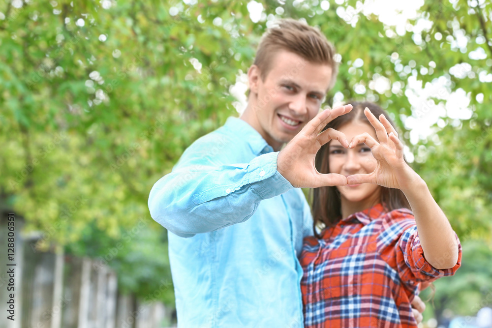 Beautiful young couple outdoors using hands to form heart
