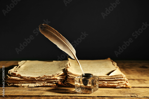 Feather pen with inkwell and stack of papers on dark background photo