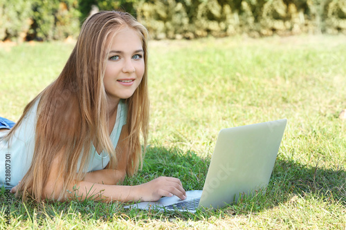 Pretty teenager girl lying on green lawn with laptop
