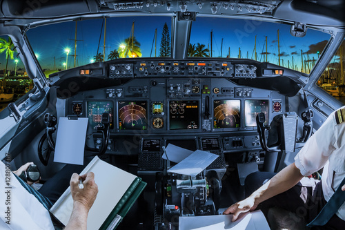 Airplane cockpit flying on Ala Wai Harbor, Honolulu by night, Oahu, Hawaii, with pilots arms and blank white papers for copy space.