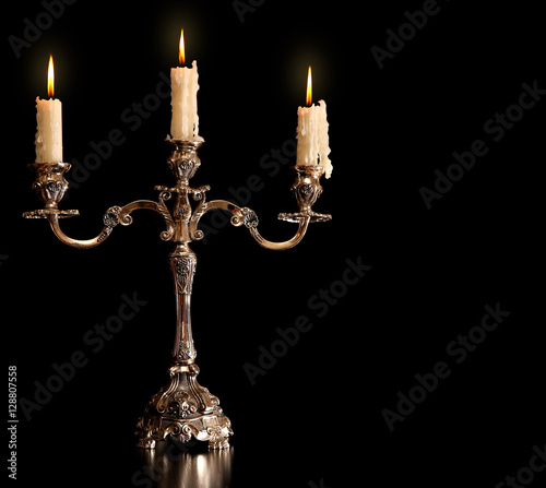 burning old candle vintage bronze Silver candlestick. Isolated Black Background.