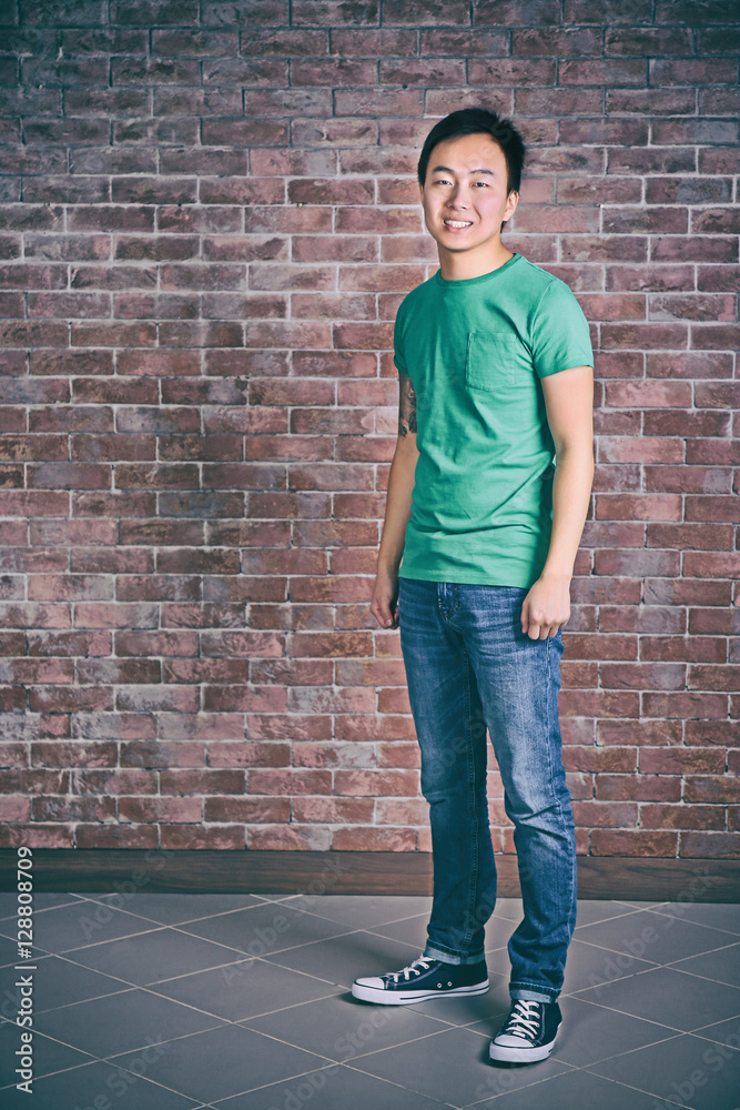 Asian man in blank green t-shirt standing against brick wall Asian man in blank green t-shirt standing against brick wall