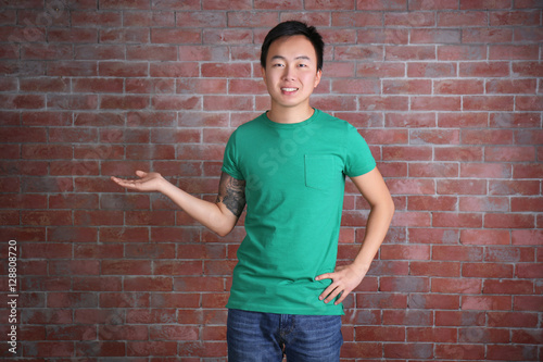 Asian man in blank green t-shirt standing against brick wall