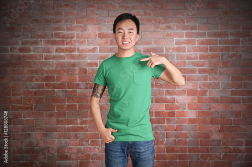 Asian man in blank green t-shirt standing against brick wall