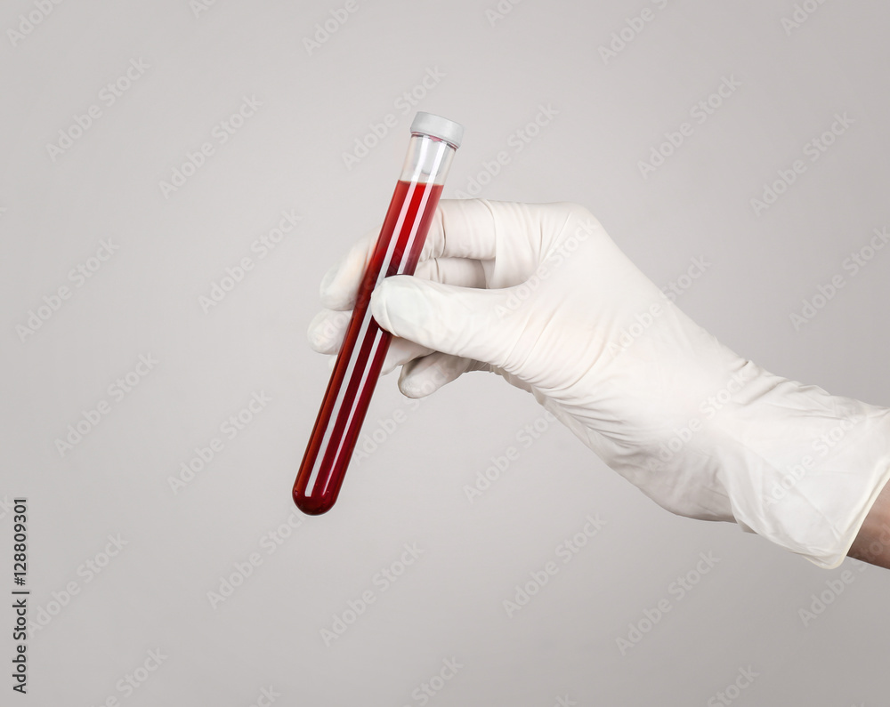 Hand of a doctor holding red blood in test tube on gray background, close up Hand of a doctor holding red blood in test tube on gray background, close up