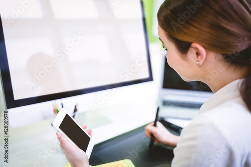 Graphic designer holding phone while working at desk