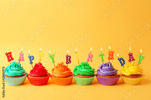 Tasty colorful cupcakes with Happy Birthday candles on yellow background