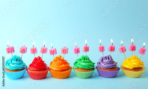 Tasty colorful cupcakes with Happy Birthday candles on blue background