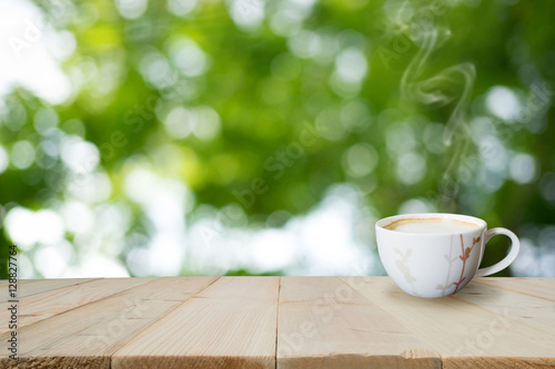A cup of cappuccino on old wooden floor or wooden table with blur background is light streaming through leaves.