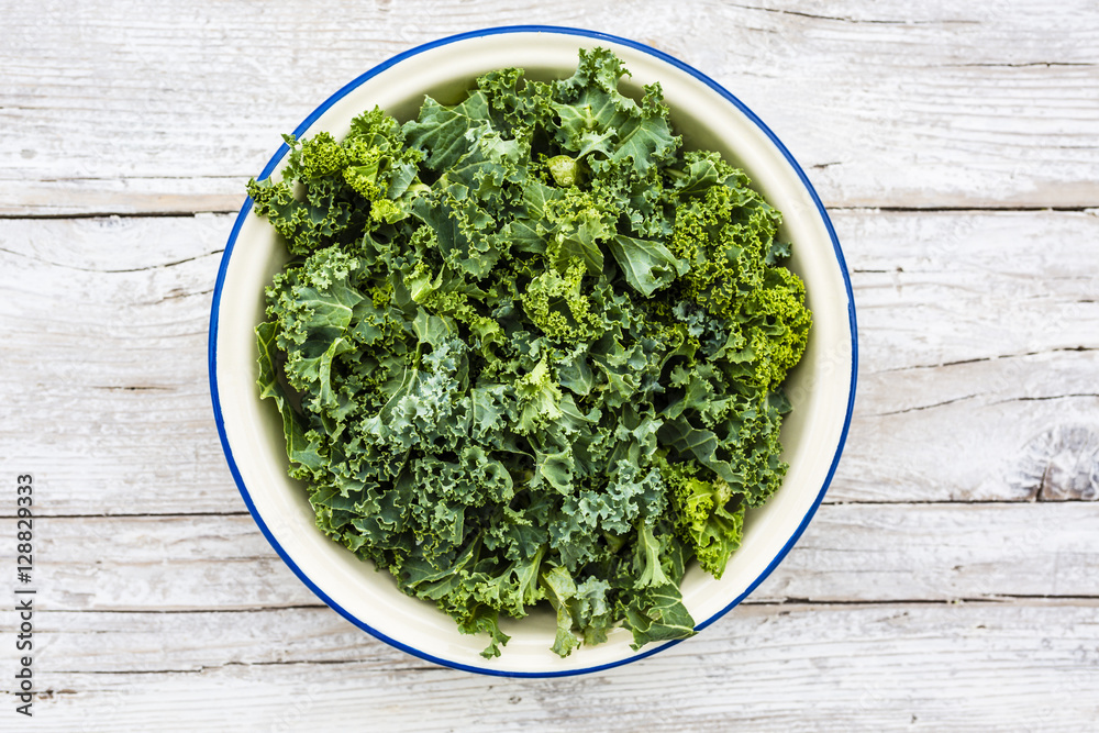 Fresh and raw kale leaves in a bowl on a wooden background. Fresh and raw kale leaves in a bowl on a wooden background.