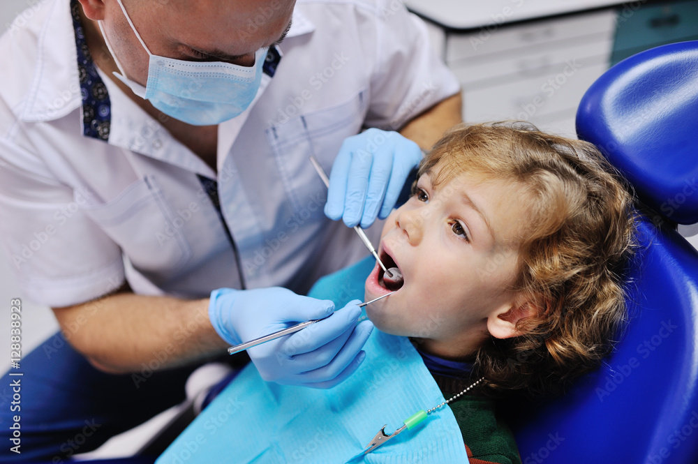 Male dentist examines the teeth of the patient cheerful child with curly red hair. Moloi boy smiling in dentist's chair. child mouth wide open in the dentist's chair Male dentist examines the teeth of the patient cheerful child with curly red hair. Moloi boy smiling in dentist's chair. child mouth wide open in the dentist's chair