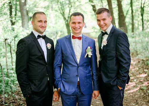 happy and young groom and his friends standing together outdoors