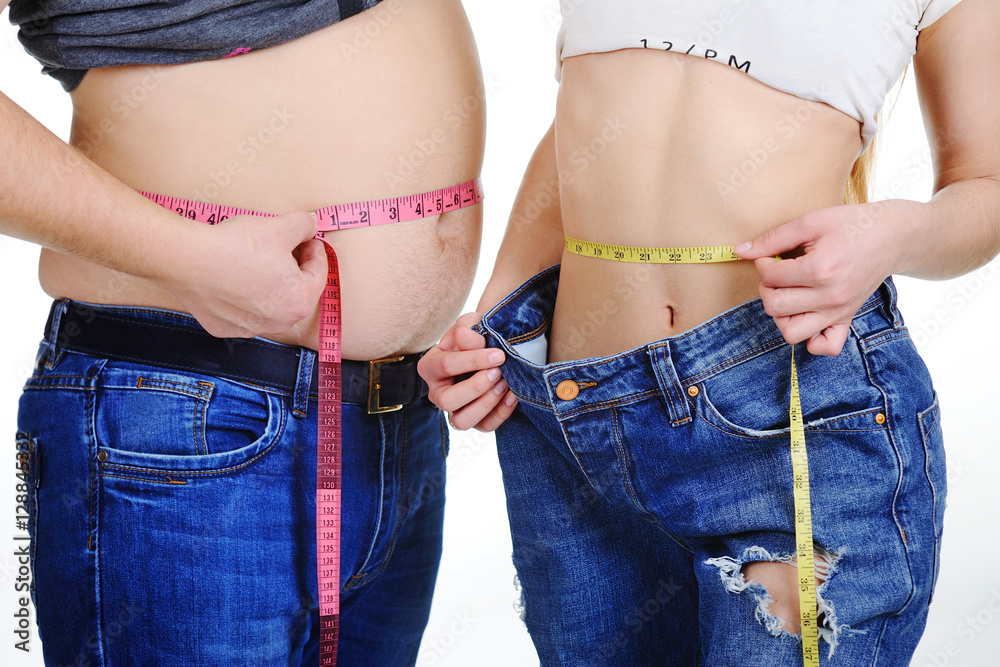 a guy with a big belly and a slim girl measuring waist measuring tape on a  white background Stock Photo