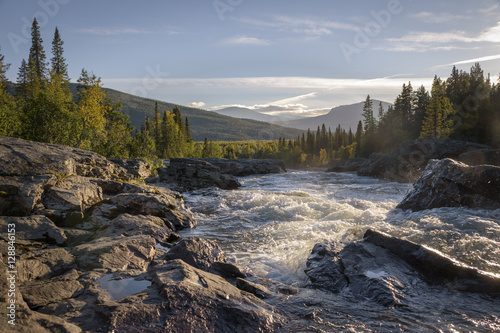Golden light shining on wild river flowing down the beautiful Swedish landscape photo