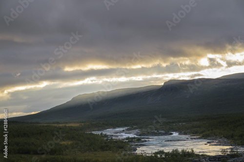Sunbeams forming over mountains on sunset giving beautiful golden light over river in Sarek, Sweden