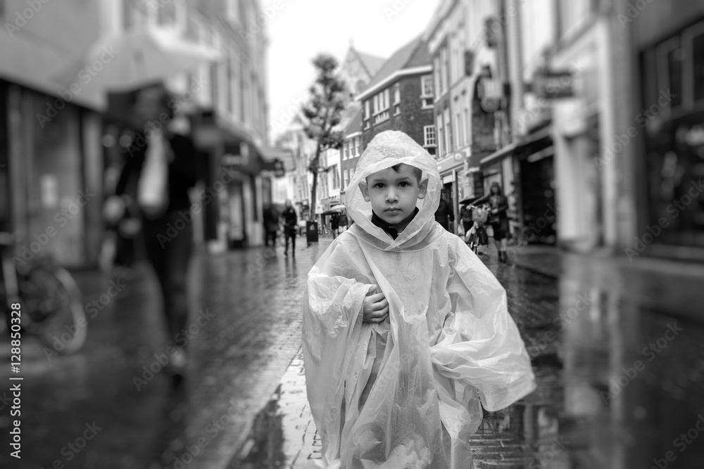 Obraz premium child with his raincoat on pebbles old city in case of rain, the Netherlands