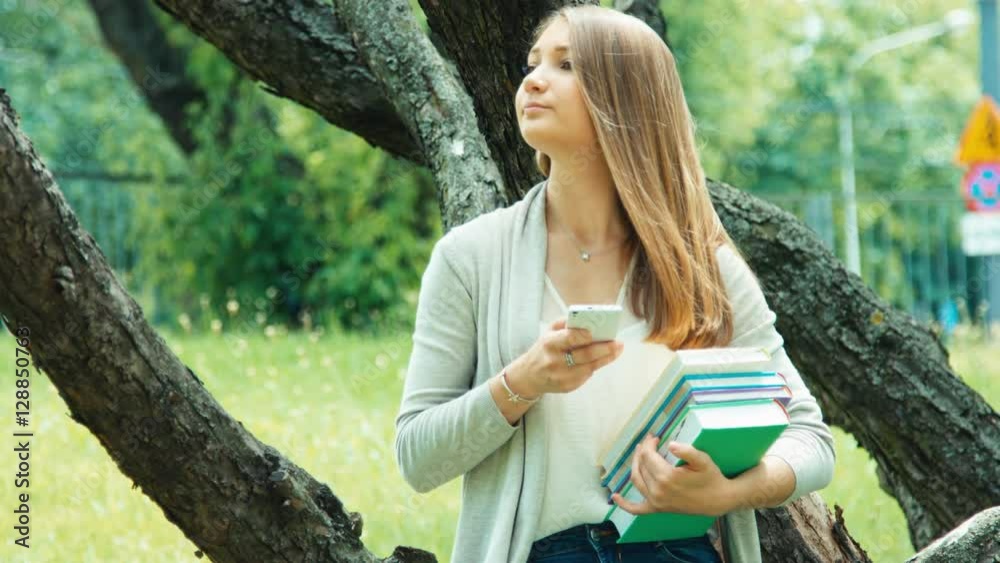 Young student typing text on cell phone holding her books and tablet outdoors Young student typing text on cell phone holding her books and tablet outdoors